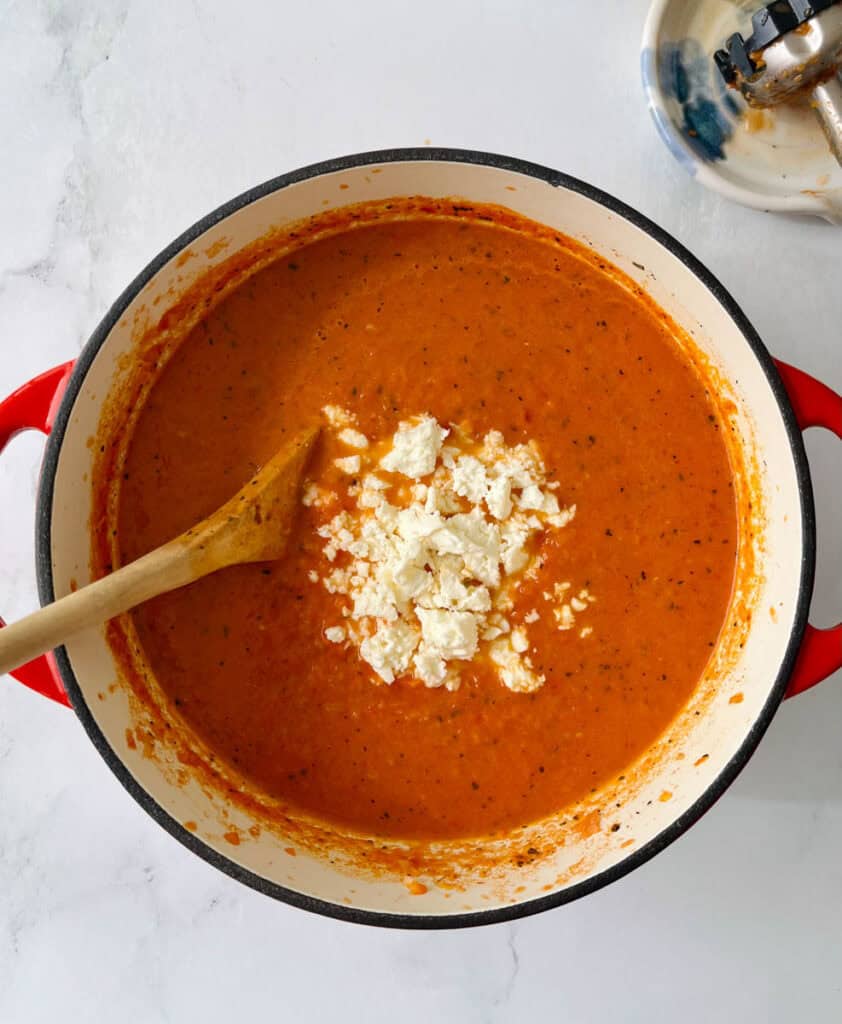 A pot of creamy tomato soup with cheese topping and a wooden spoon.