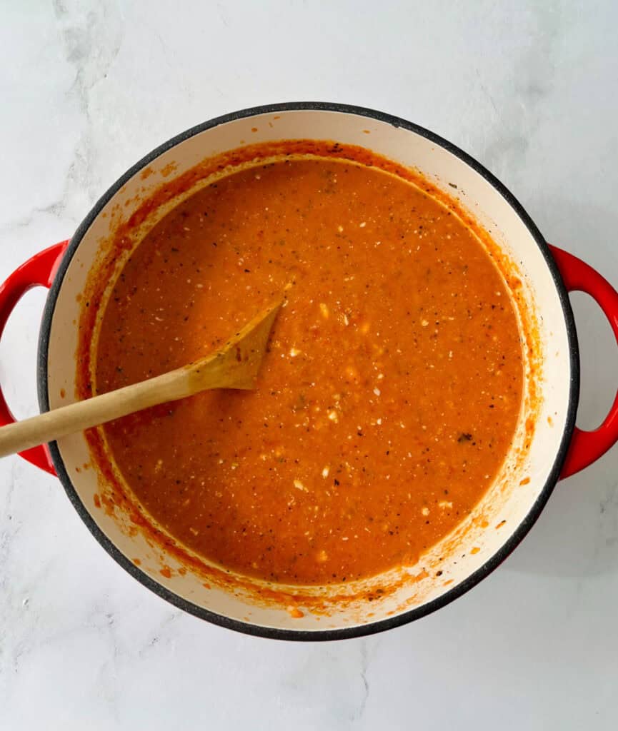Close-up of a pot of homemade tomato soup with a wooden spoon inside.