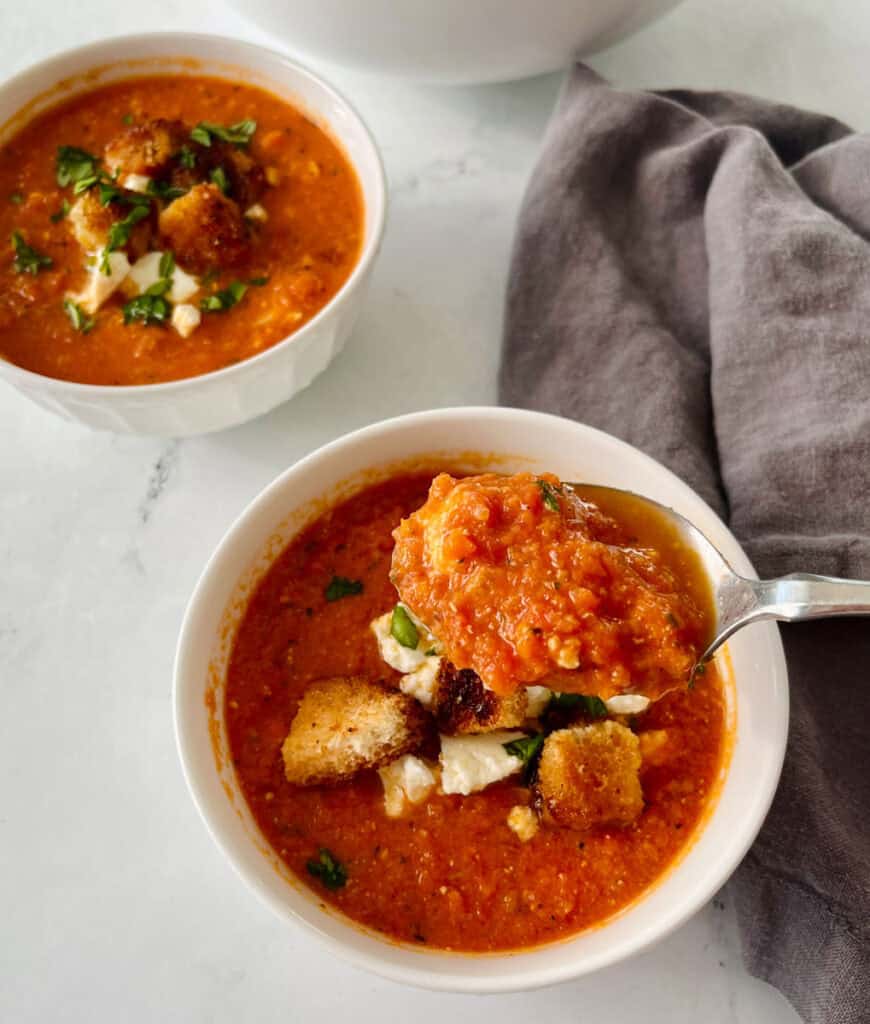 Close-up of tomato soup with croutons and herbs in a white bowl.