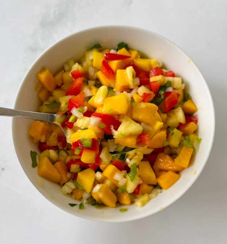 Fresh salsa with mango, pineapple, red bell pepper, and onion in a white bowl.