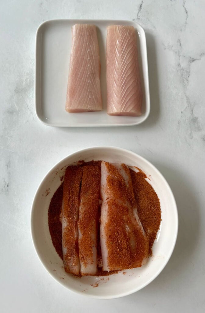 Fresh fish fillets on a white plate with spices for cooking.