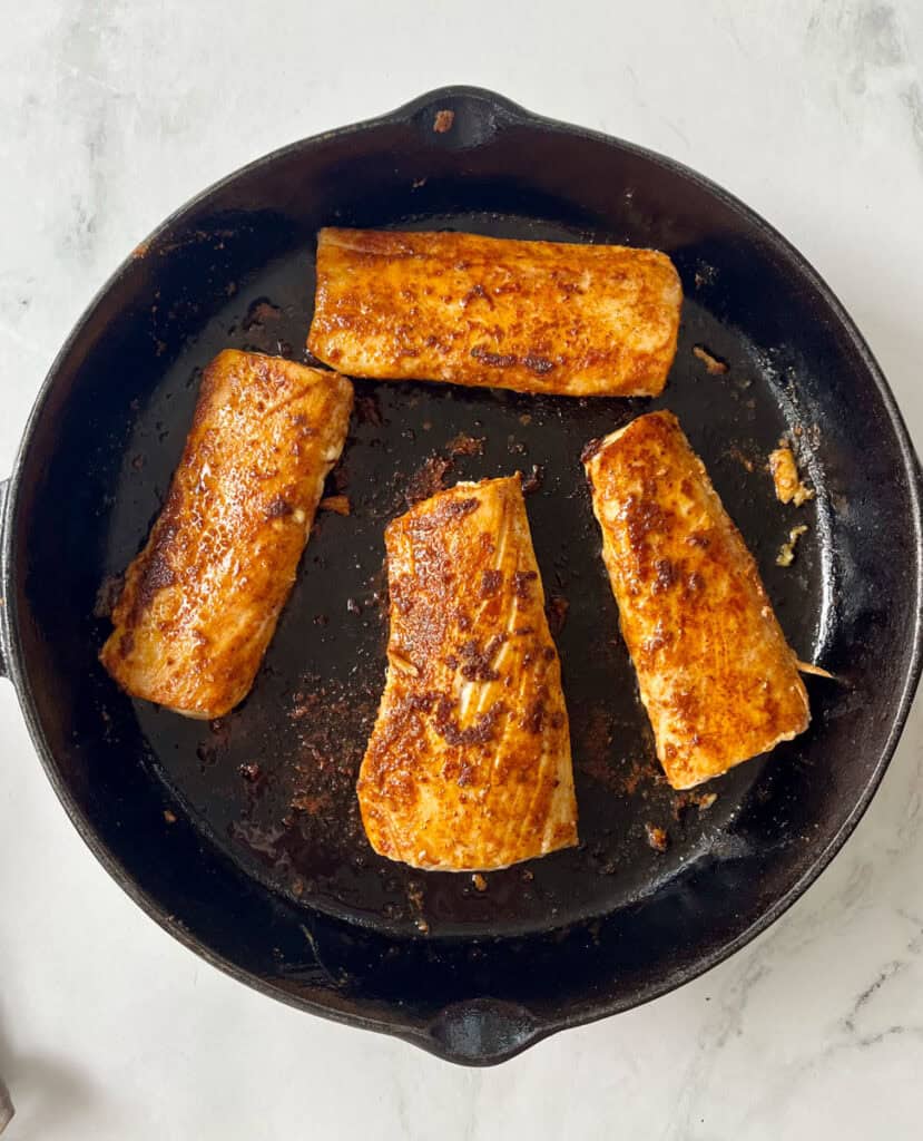 Golden-brown fish fillets in a black skillet.
