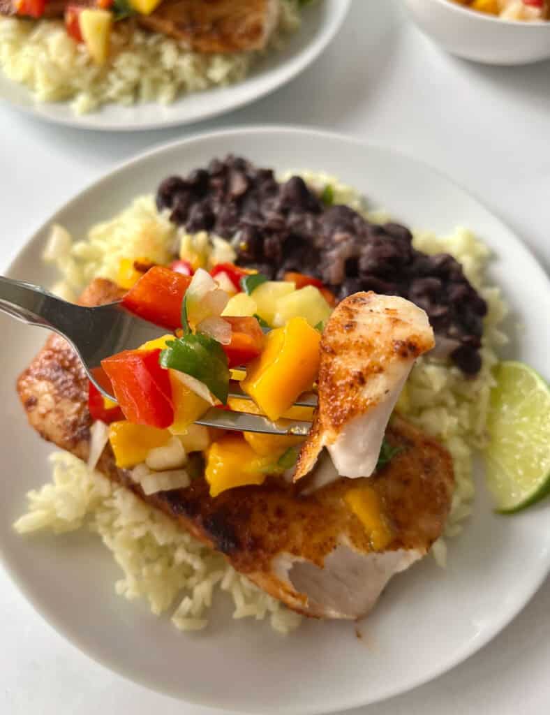 Blackened fish with rice, beans, and a colorful salsa on a white plate.