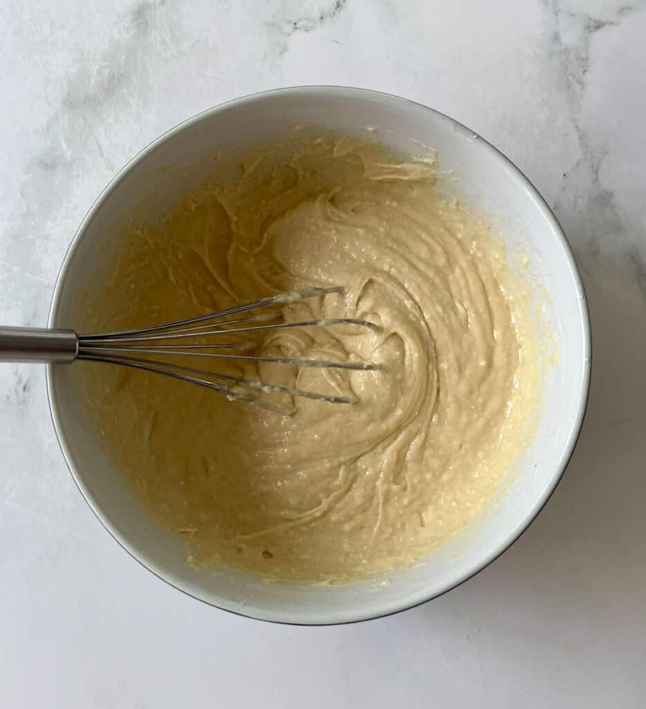 Batter being mixed in a white bowl with a whisk for baking.
