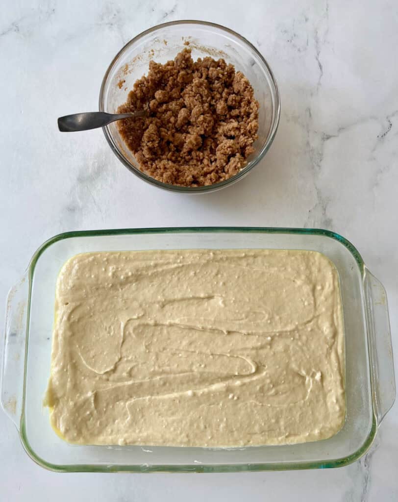 Coffee cake batter in a glass dish with crumb topping in a bowl near by.