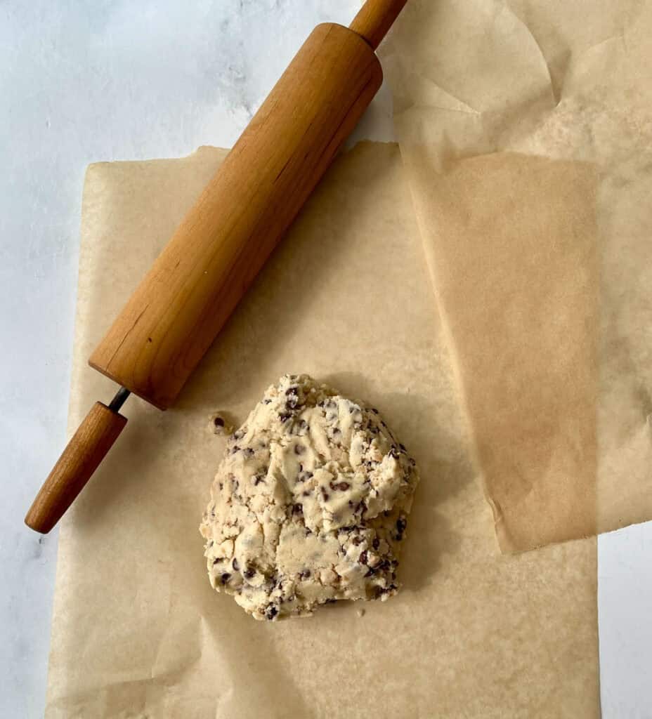 Shortbread with chocolate chip and toffee bits cookie dough with rolling pin on parchment paper for baking.