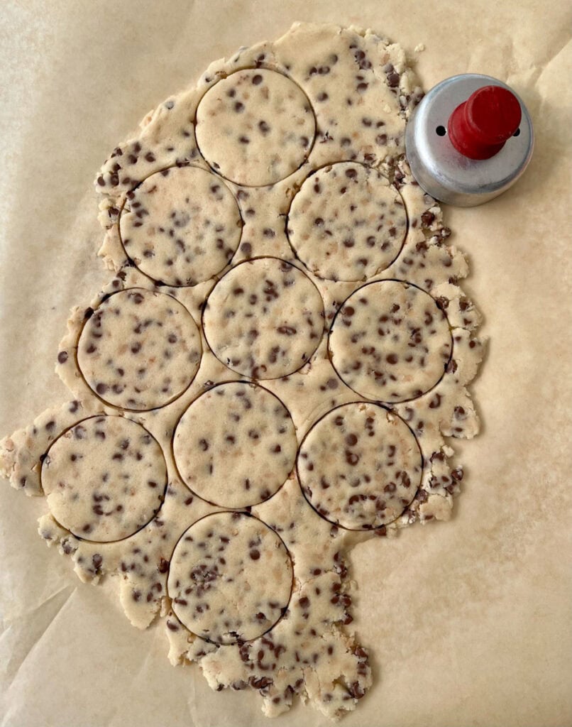 Shortbread cookie dough with chocolate chips and toffee bits and cookie cutter on parchment paper.
