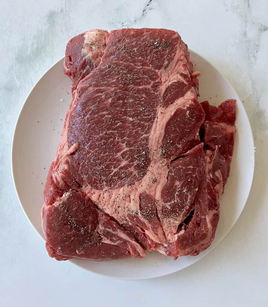 Fresh raw seasoned beef roast on white plate for cooking or grilling.