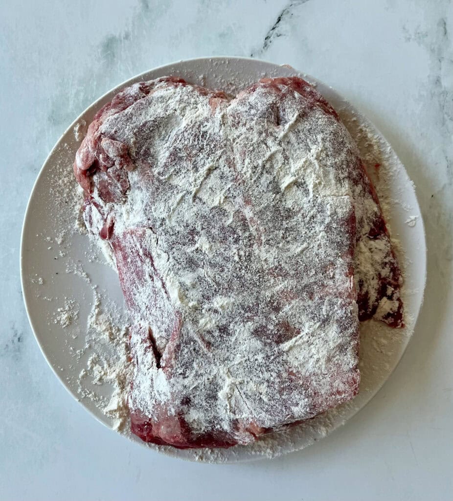 Raw beef cut on a white plate with flour, ready for cooking or roasting.