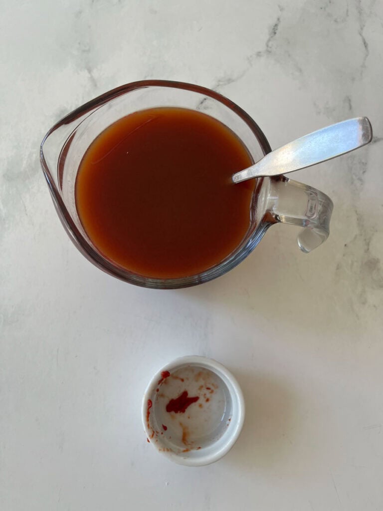 Beef broth in a glass measuring cup with a metal spoon.
