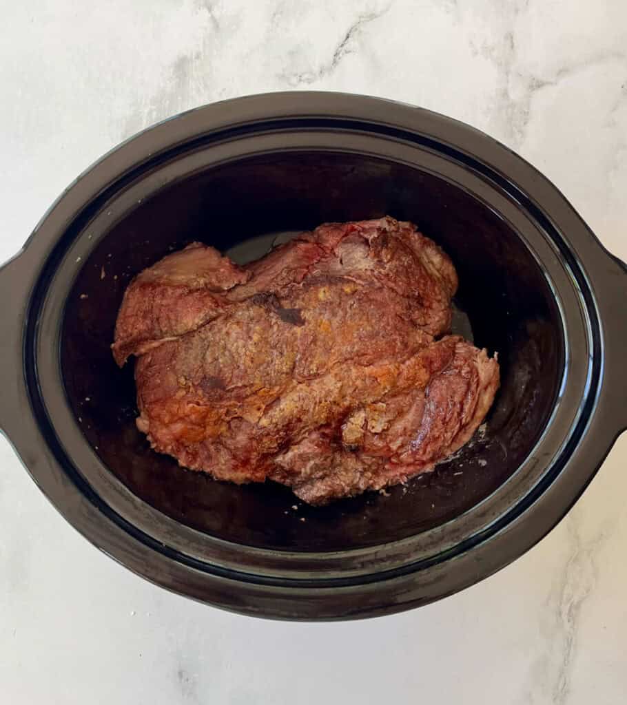 Seared beef roast in a slow cooker ready to cook.