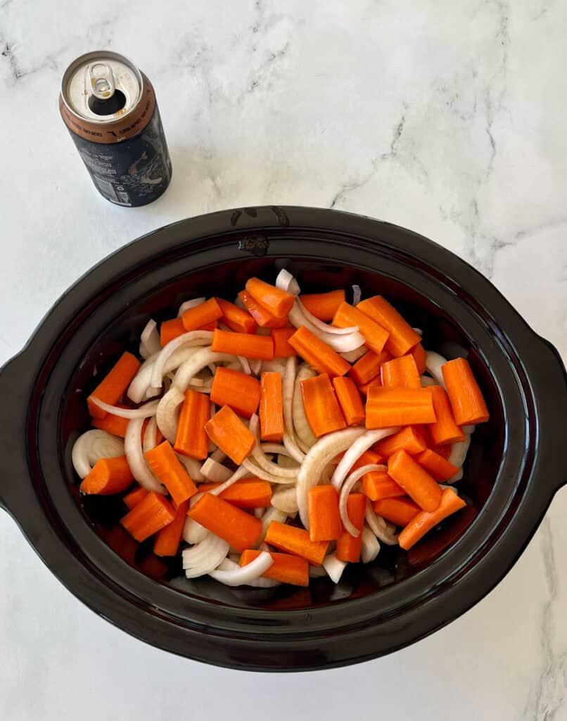 Chopped carrots and onions in a slow cooker for meal preparation.