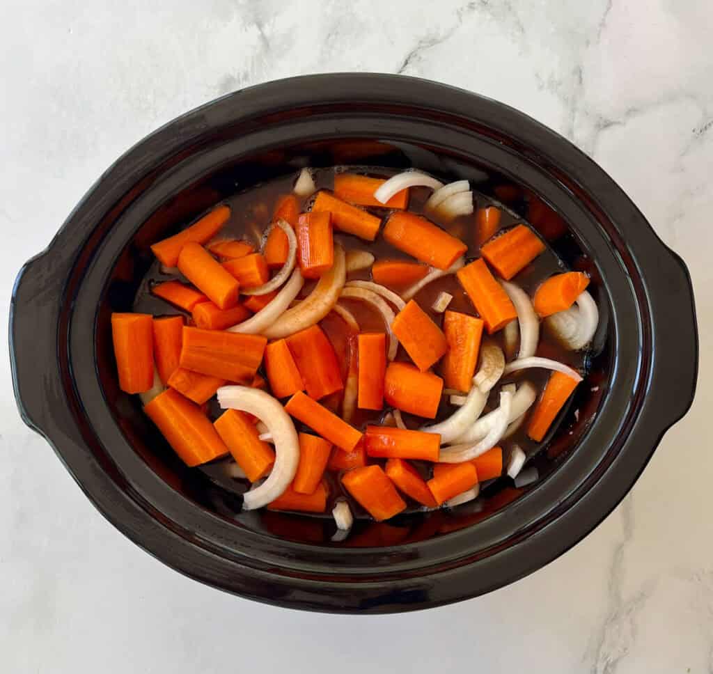 Chopped carrots and onions in a black slow cooker ready for cooking.