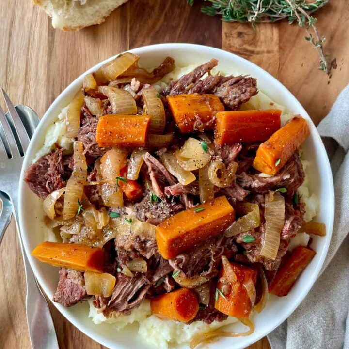 A bowl of hearty pot roast with carrots, onions, and tender beef chunks.