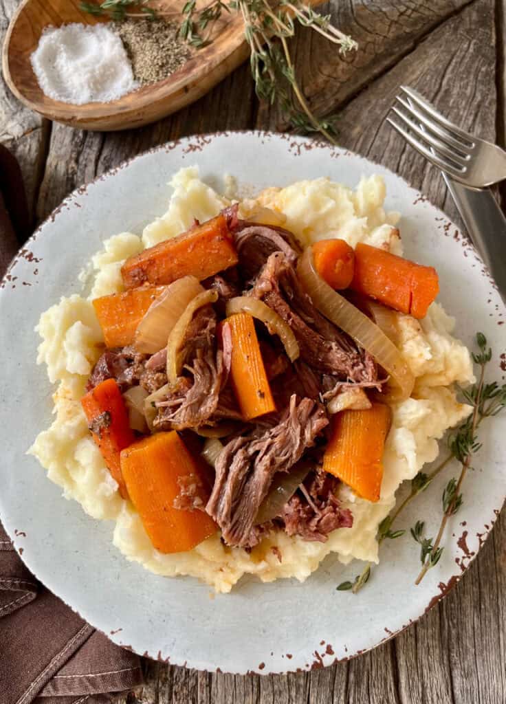 Hearty beef pot roast served over mashed potatoes with carrots and onions.