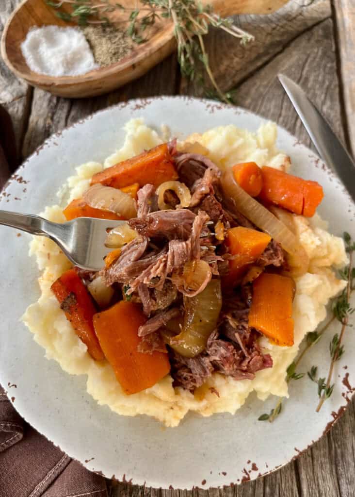 Hearty beef pot roast served over mashed potatoes with carrots and onions.