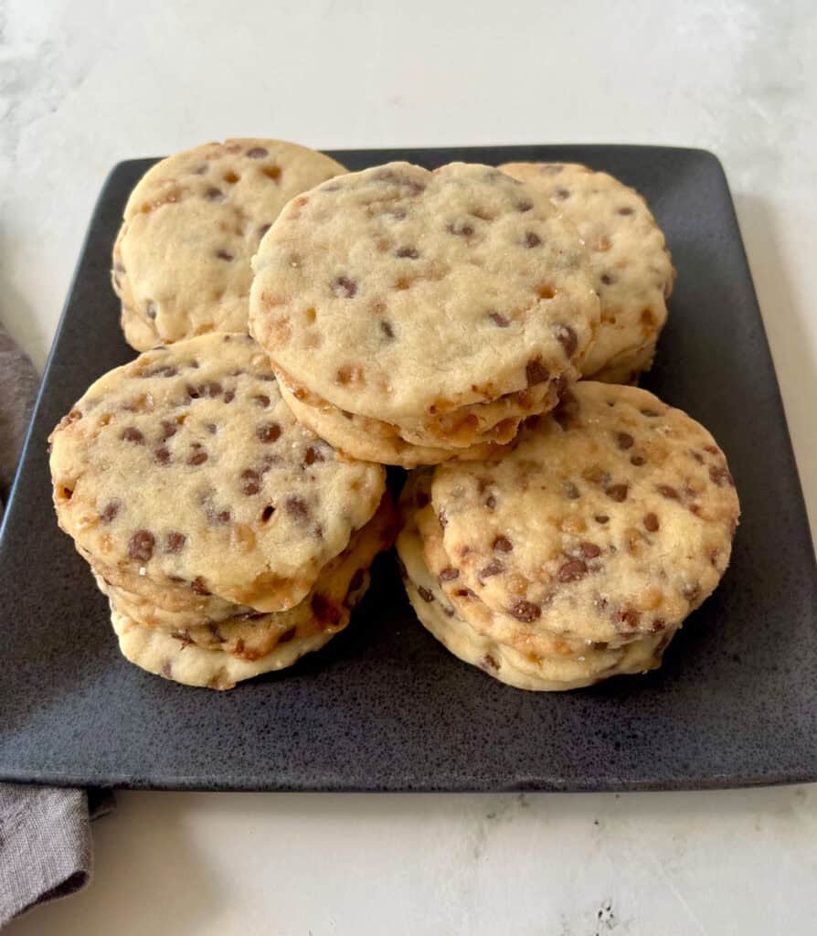Stack of homemade shortbread cookies with chocolate chips and toffee bits on black square plate.
