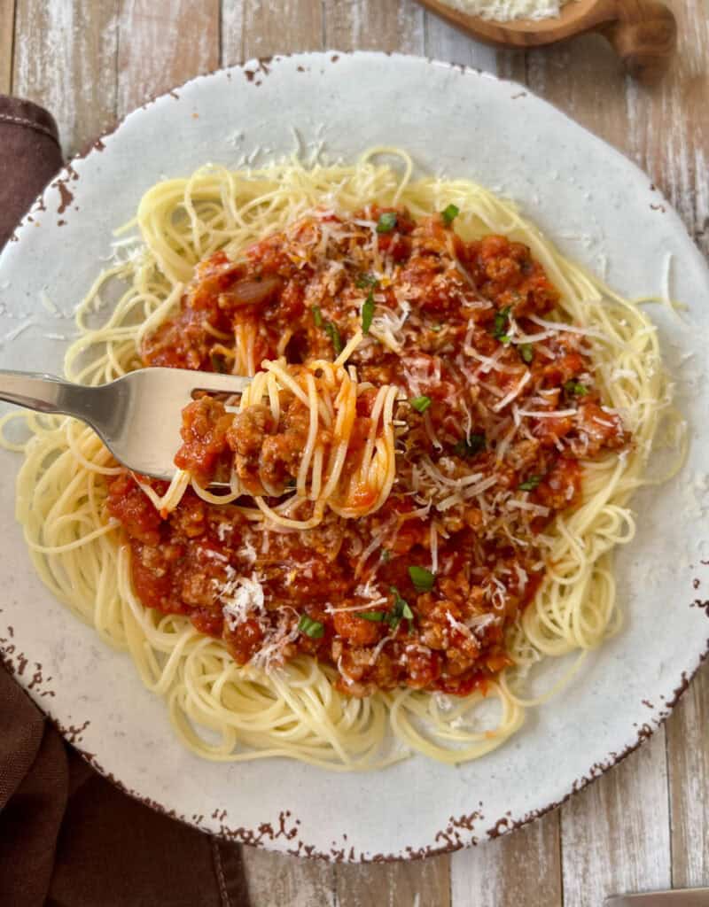 Plate of spaghetti with rich meat sauce and grated cheese.