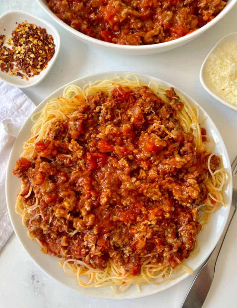 Plate of spaghetti with rich meat sauce and grated cheese.