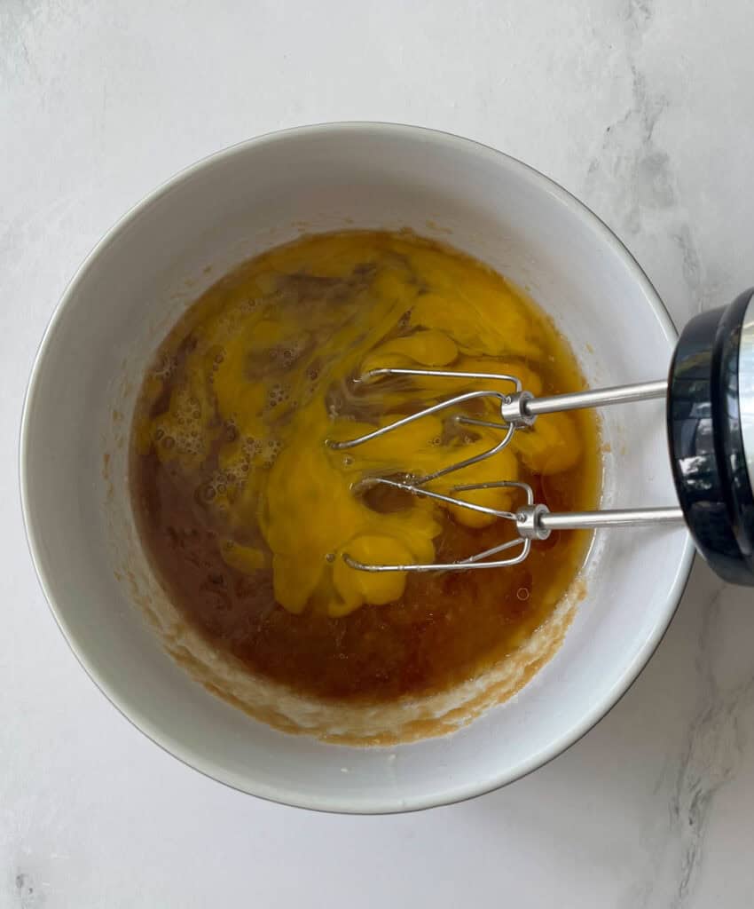 Eggs being whisked in a white bowl with a hand mixer.