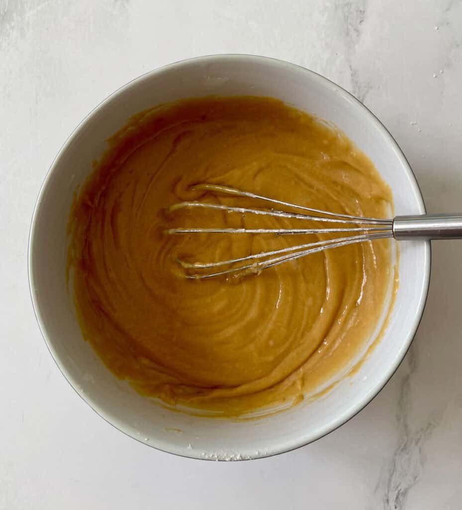 Creamy caramel batter in a white bowl with a whisk.