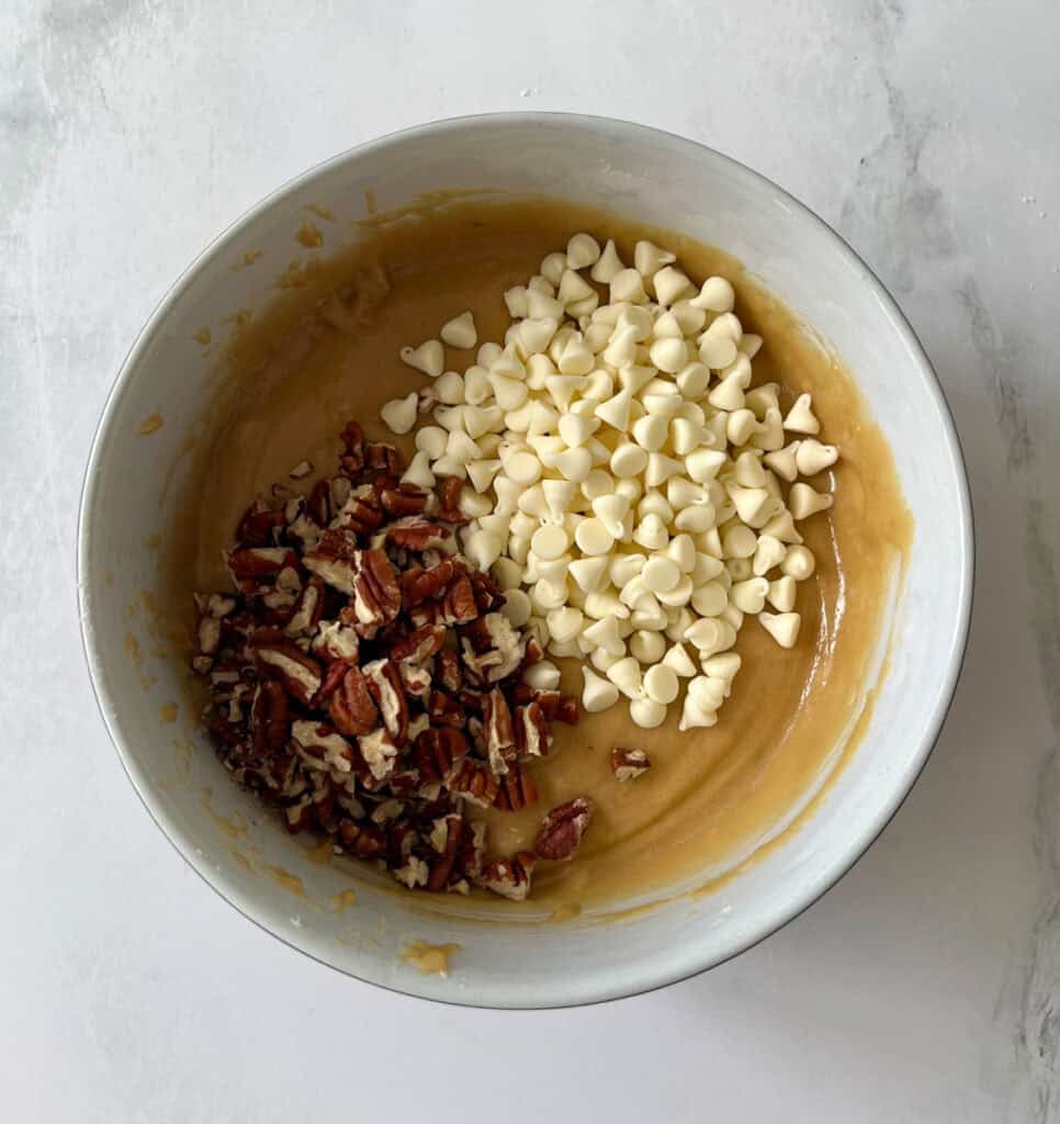 Brownie dough with chopped nuts and white chocolate chips in a mixing bowl.