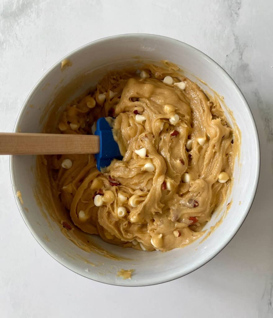Close-up of cookie dough with chocolate chips and chopped nuts in a white bowl.