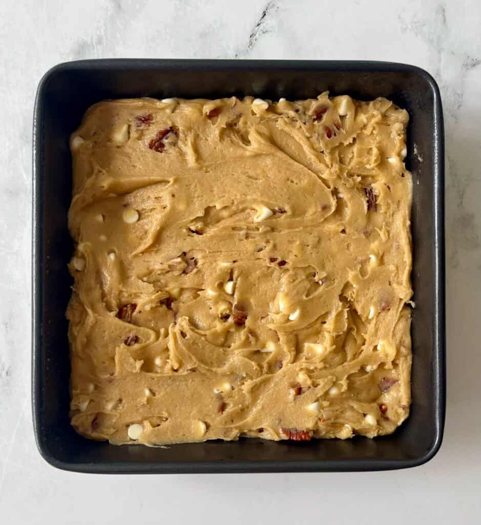 Square baking pan filled with homemade brownie dough with white chocolate chips and chopped nuts.