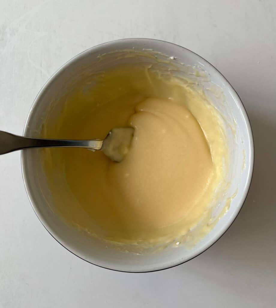 Smooth, creamy maple sauce in a white mixing bowl with a spoon.