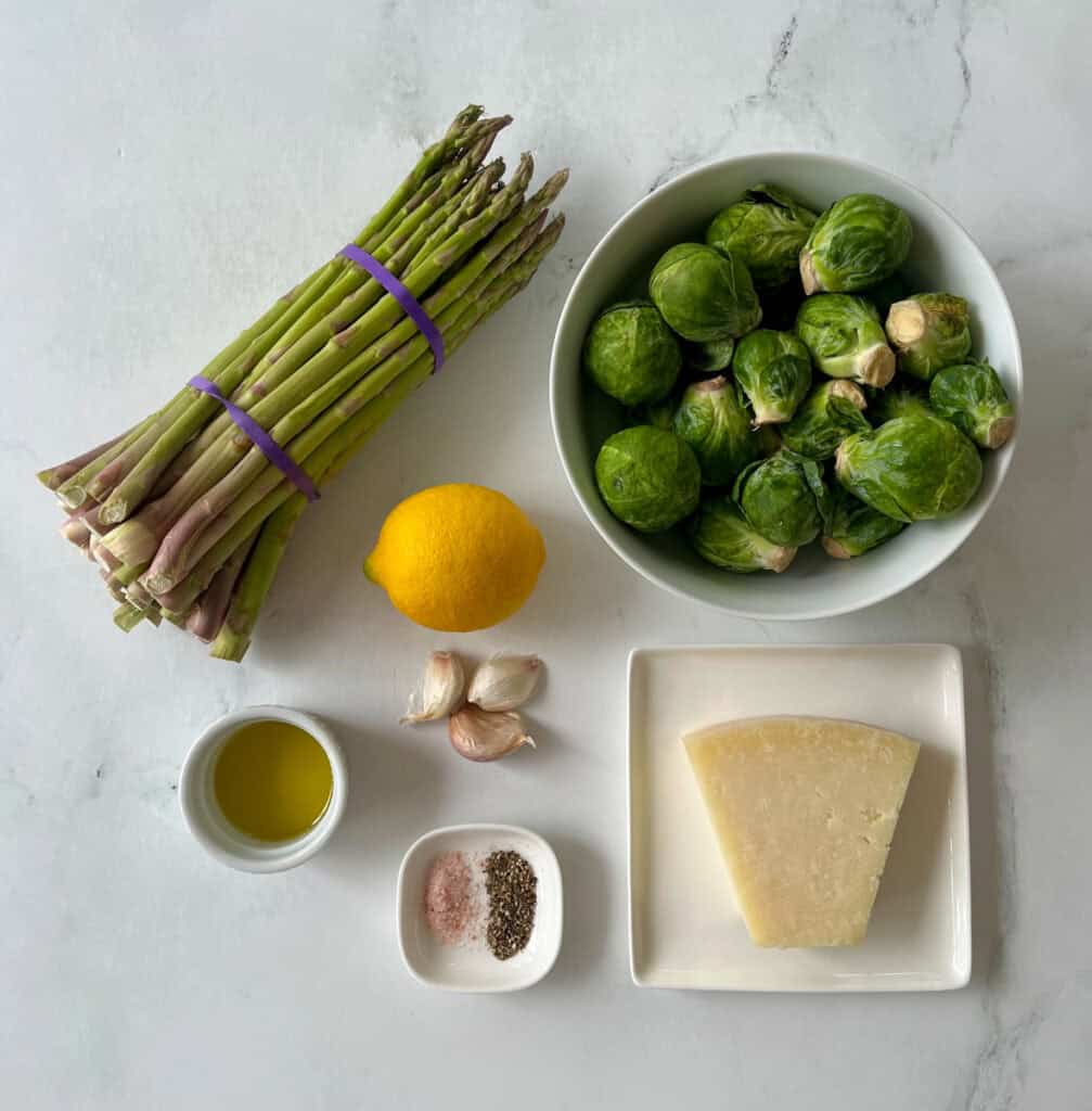 Fresh Brussels sprouts and asparagus with lemon, garlic, and cheese on a white surface.