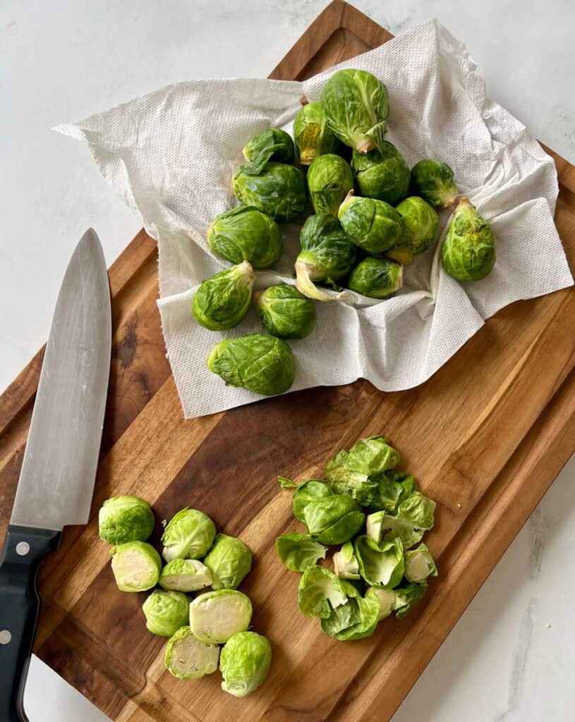 Raw Brussels sprouts on a wooden cutting board with a knife.