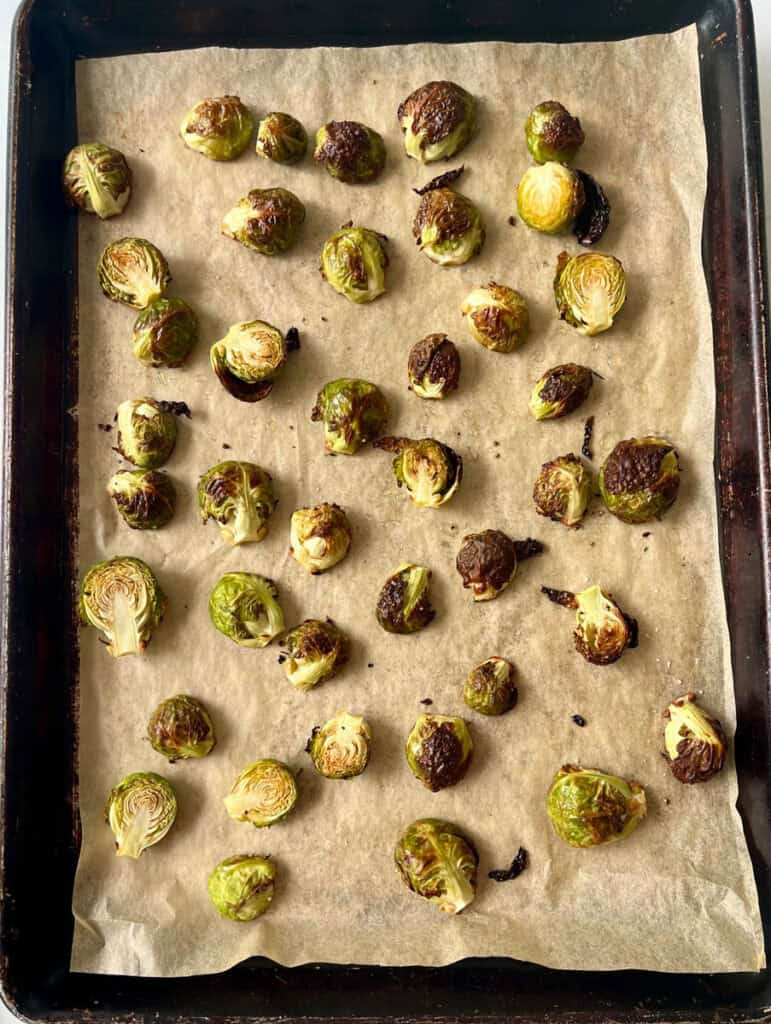 Fresh Brussels sprouts partially roasted on baking sheet with caramelized edges.