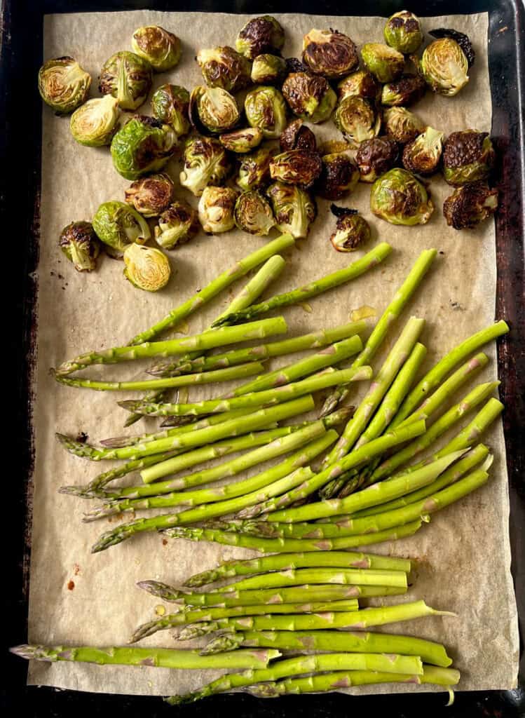 Partially roasted Brussels sprouts and asparagus on baking sheet for roasting.