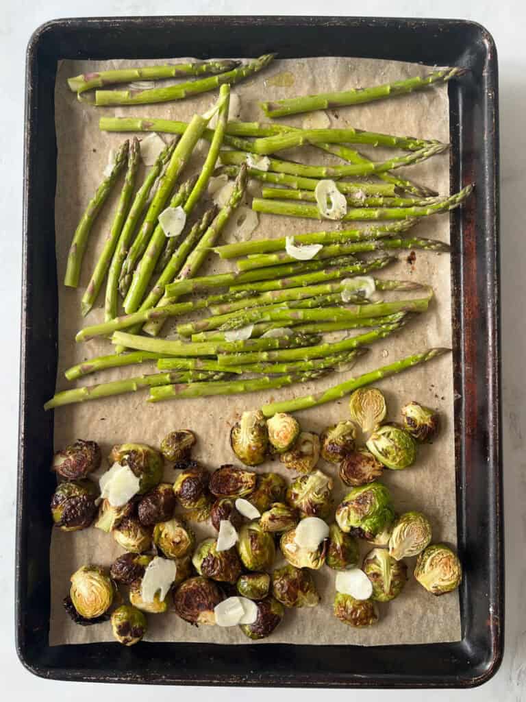 Partially roasted Brussels sprouts and raw asparagus on a baking sheet.