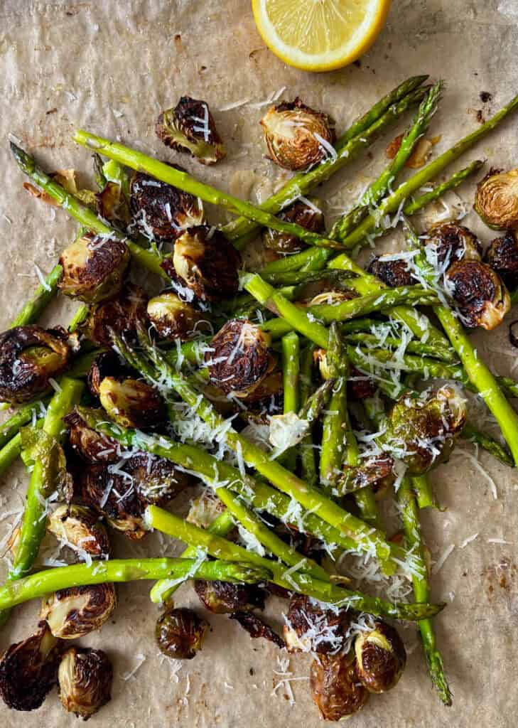 Roasted asparagus with Brussels sprouts, garlic, lemon, and grated cheese on parchment paper.