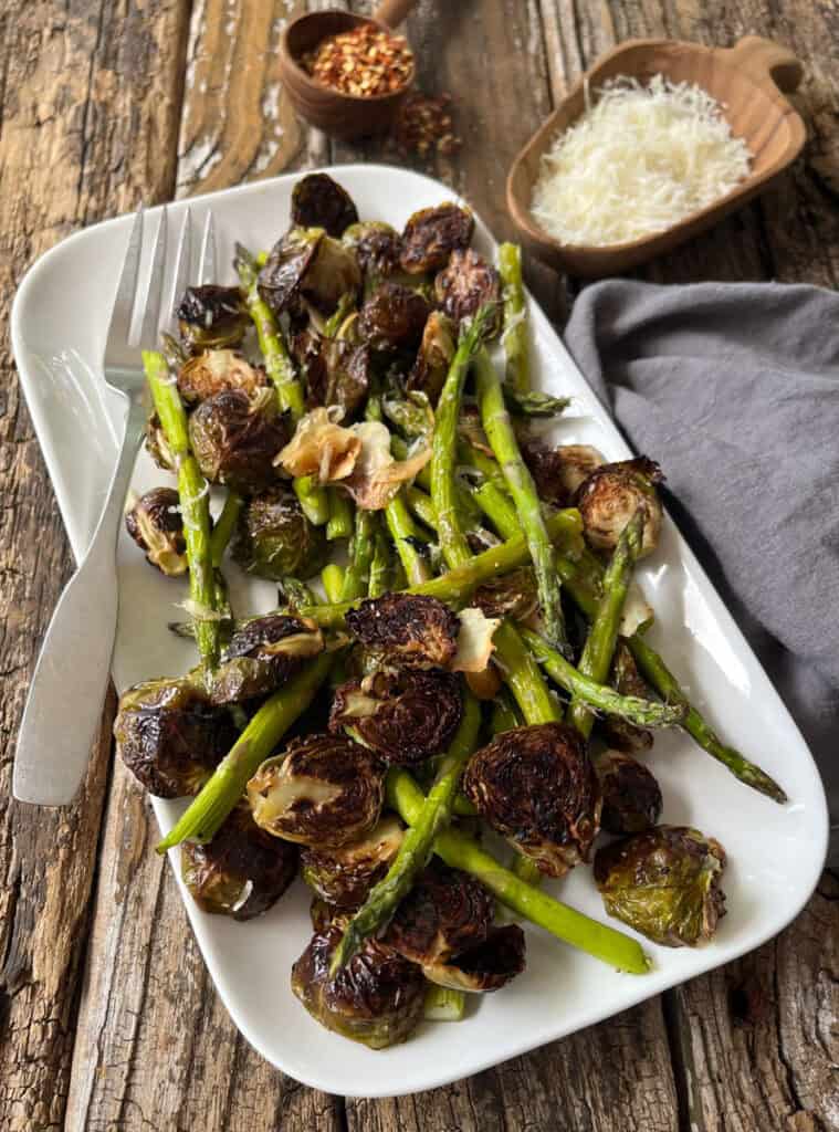 Roasted Brussels sprouts and asparagus on a white platter with grated cheese.