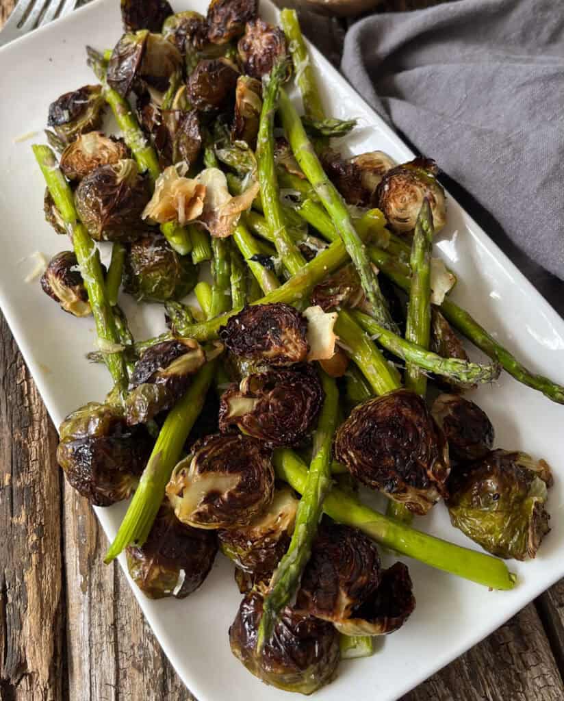 Roasted Brussels sprouts and asparagus on a white platter for healthy eating.