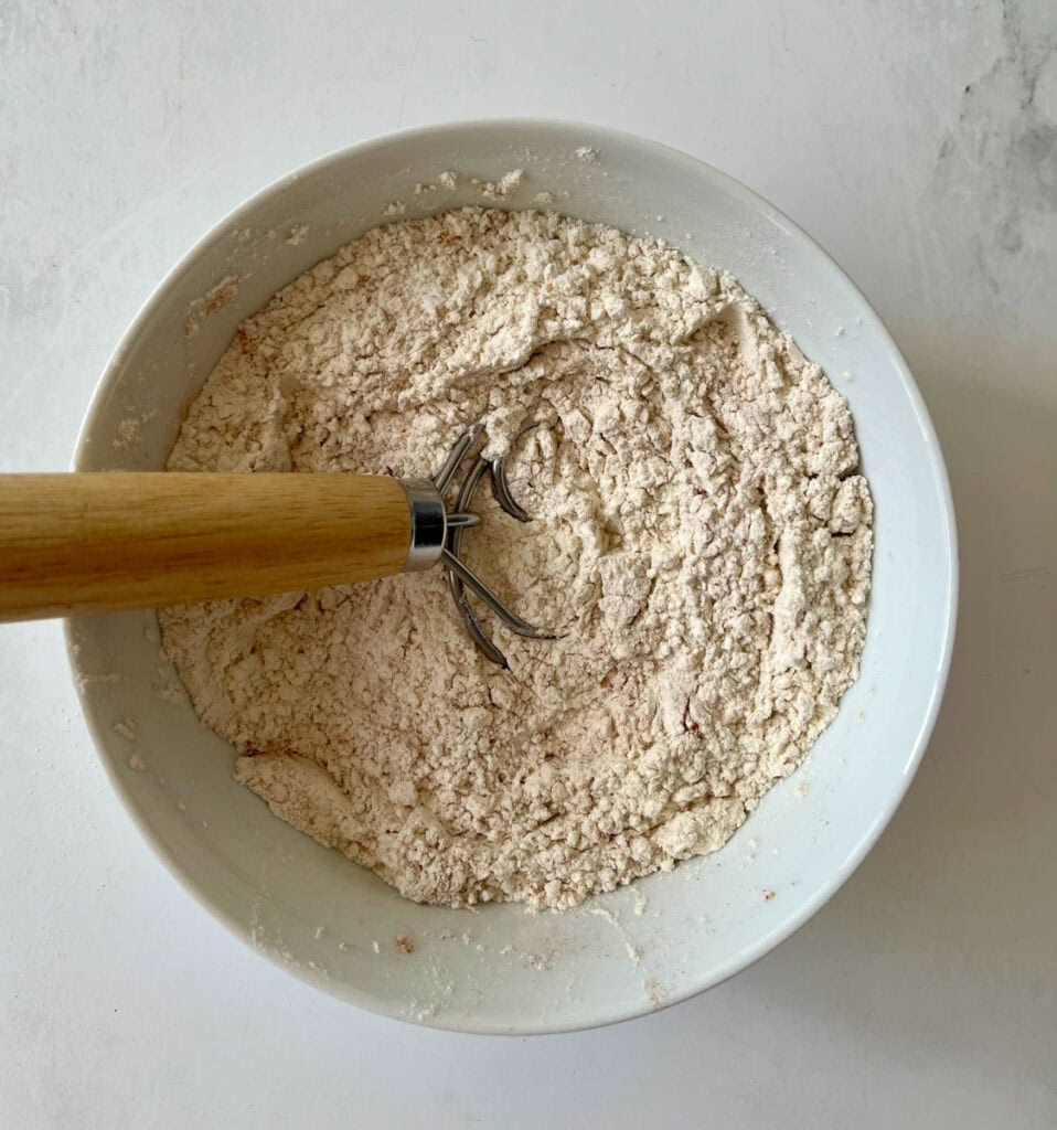 Bowl of flour with a hand mixing utensil for baking.