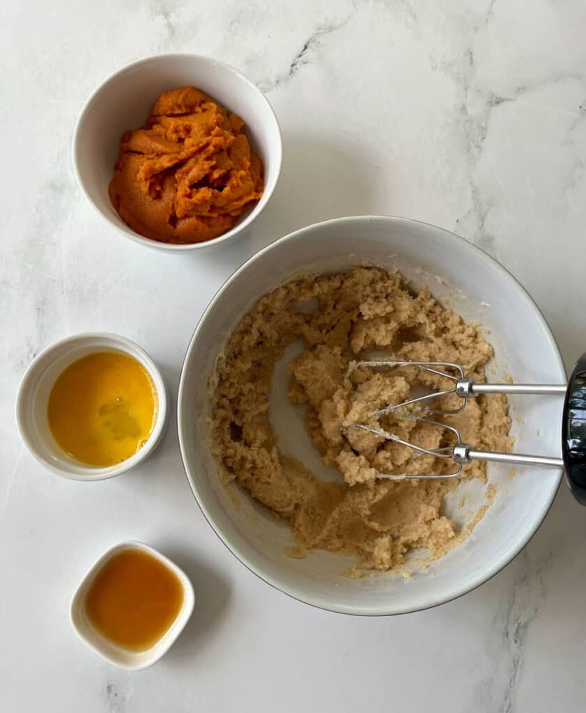 Cookie dough in a mixing bowl with ingredients nearby on a white surface.