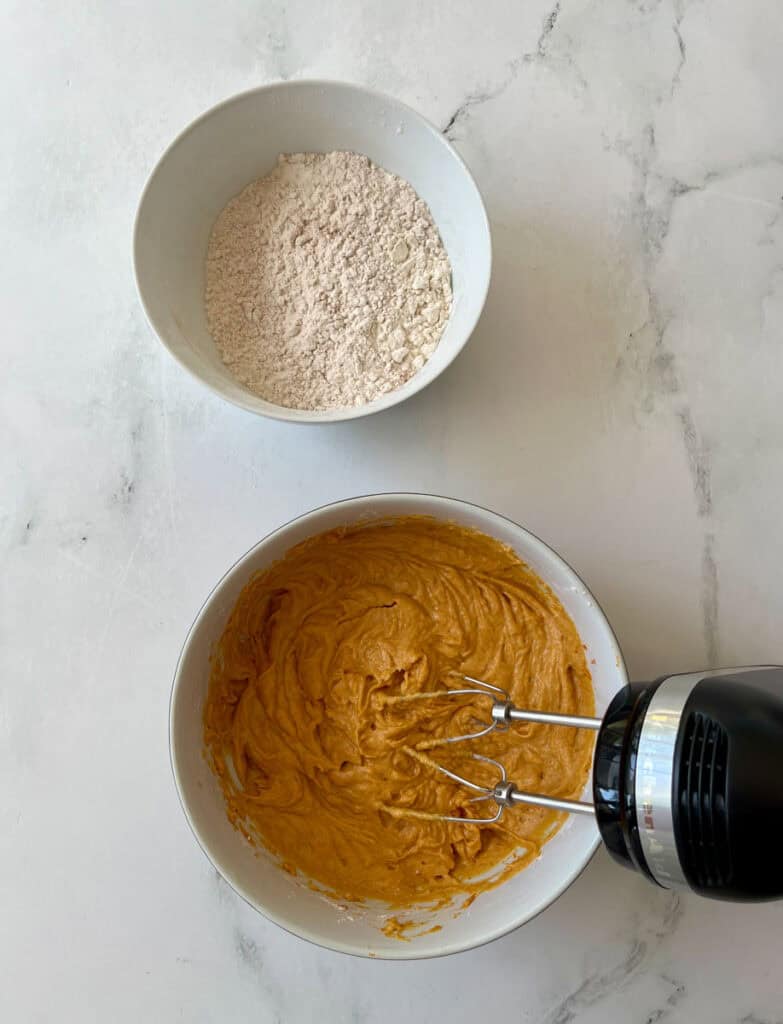 Flour mixture and pumpkin batter in bowls for baking pumpkin cookies.