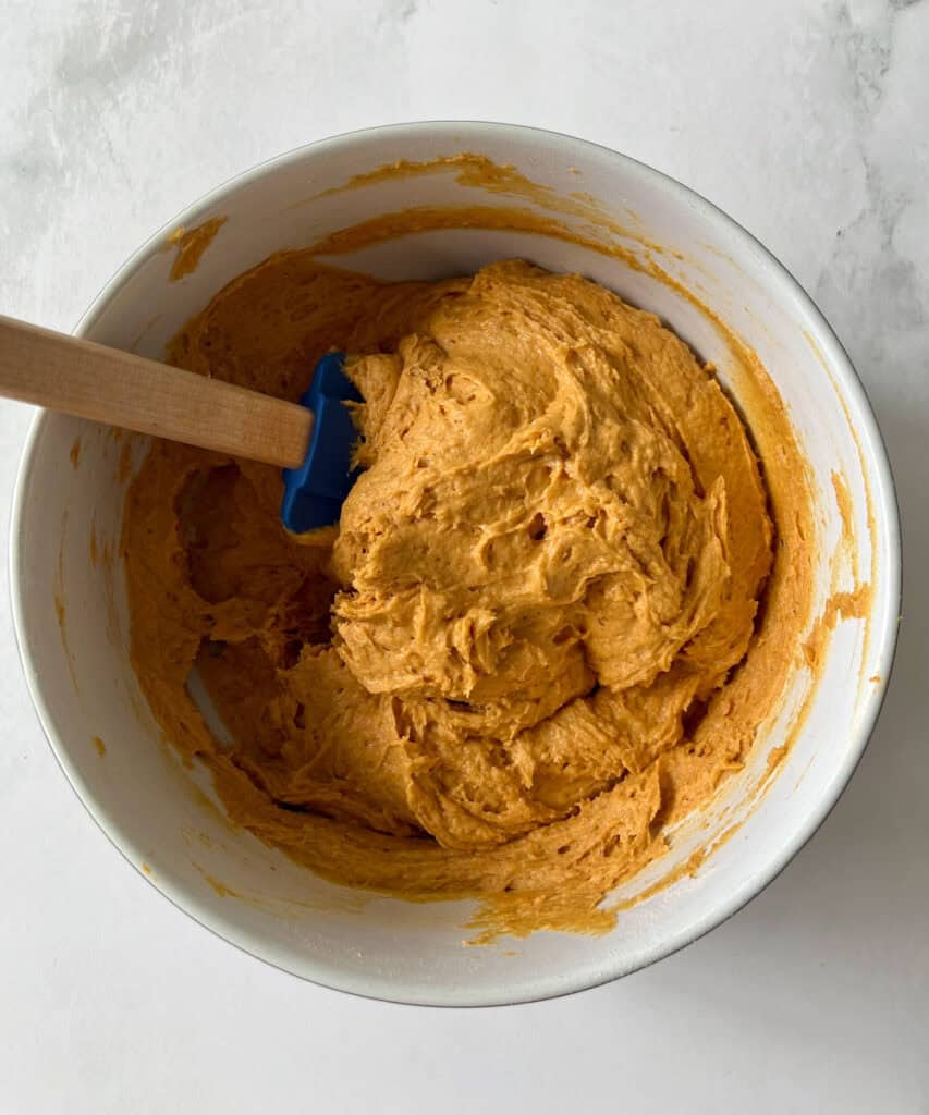 Smooth pumpkin cookie dough in a white bowl with a wooden spatula.