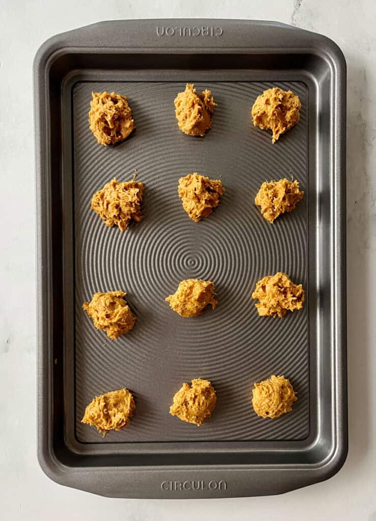 Raw cookie dough portions arranged on a baking sheet for baking.