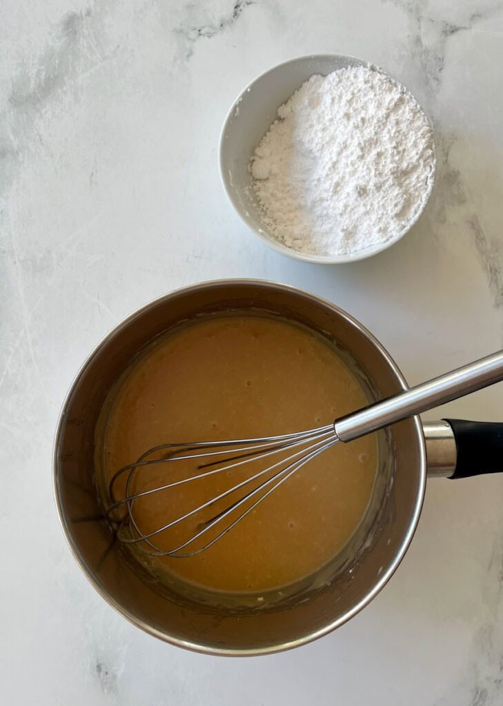 Mixing frosting in a saucepan with a whisk and powdered sugar in a bowl.
