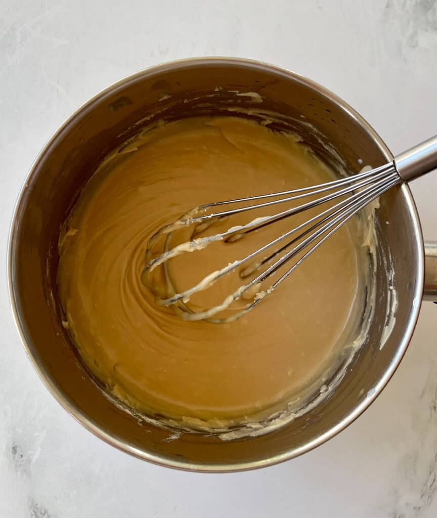 Smooth caramel sauce being mixed in a stainless steel bowl with a whisk.