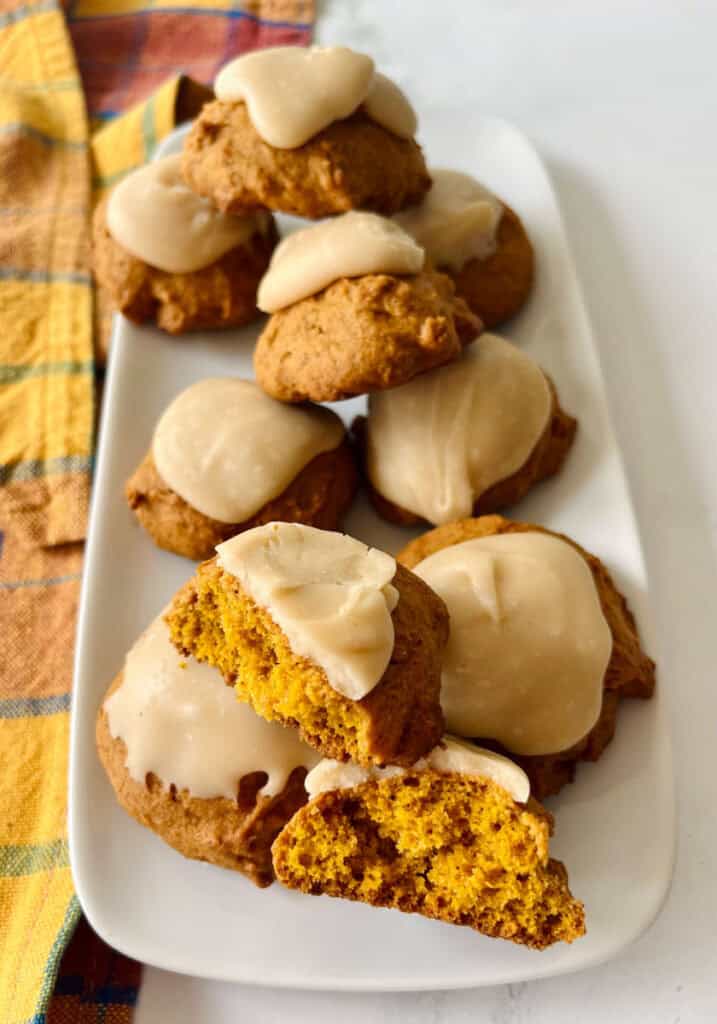 Delicious pumpkin cookies topped with creamy frosting on a white platter.