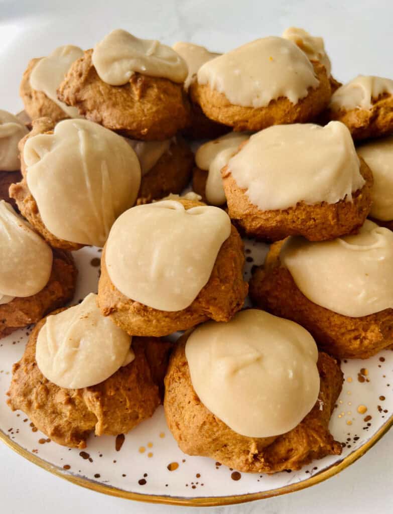 Delicious homemade pumpkin cookies topped with penuche frosting on a white plate.