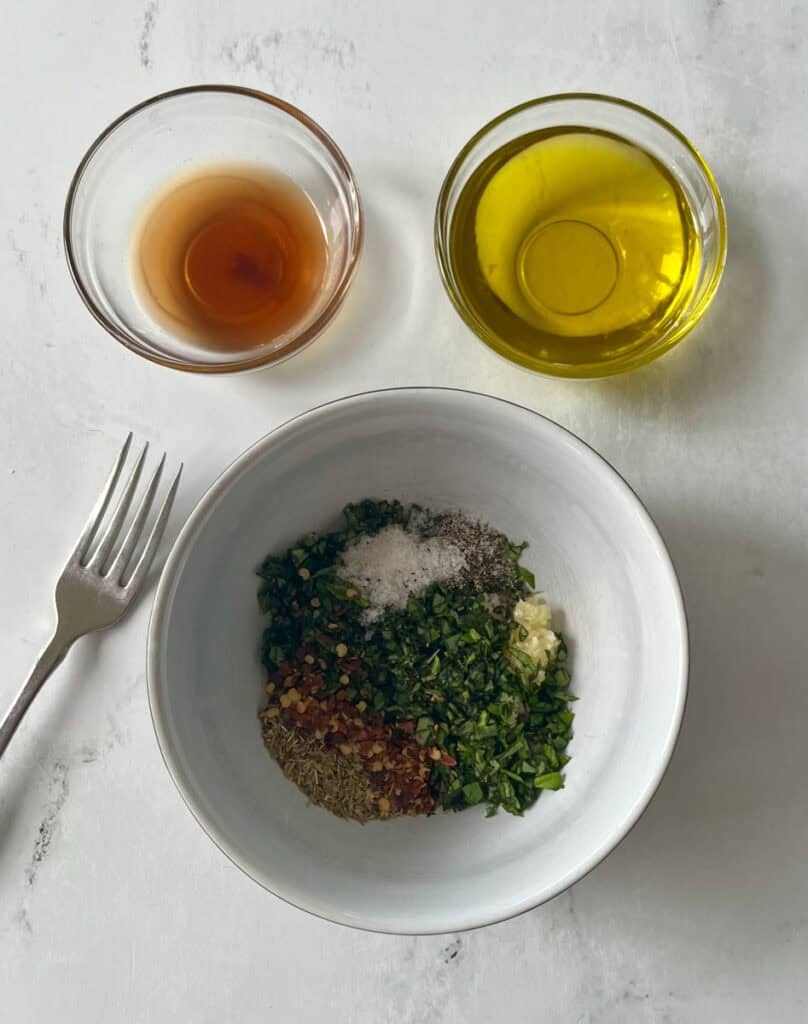 Bowls of oil, vinegar, and chopped herbs and spices for chimichurri sauce.
