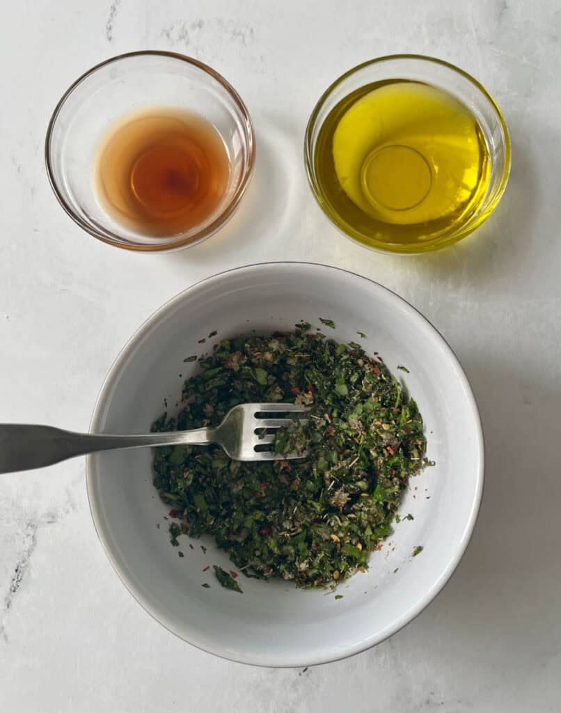 Herb mixture with olive oil and vinegar in bowls for chimichurri sauce.