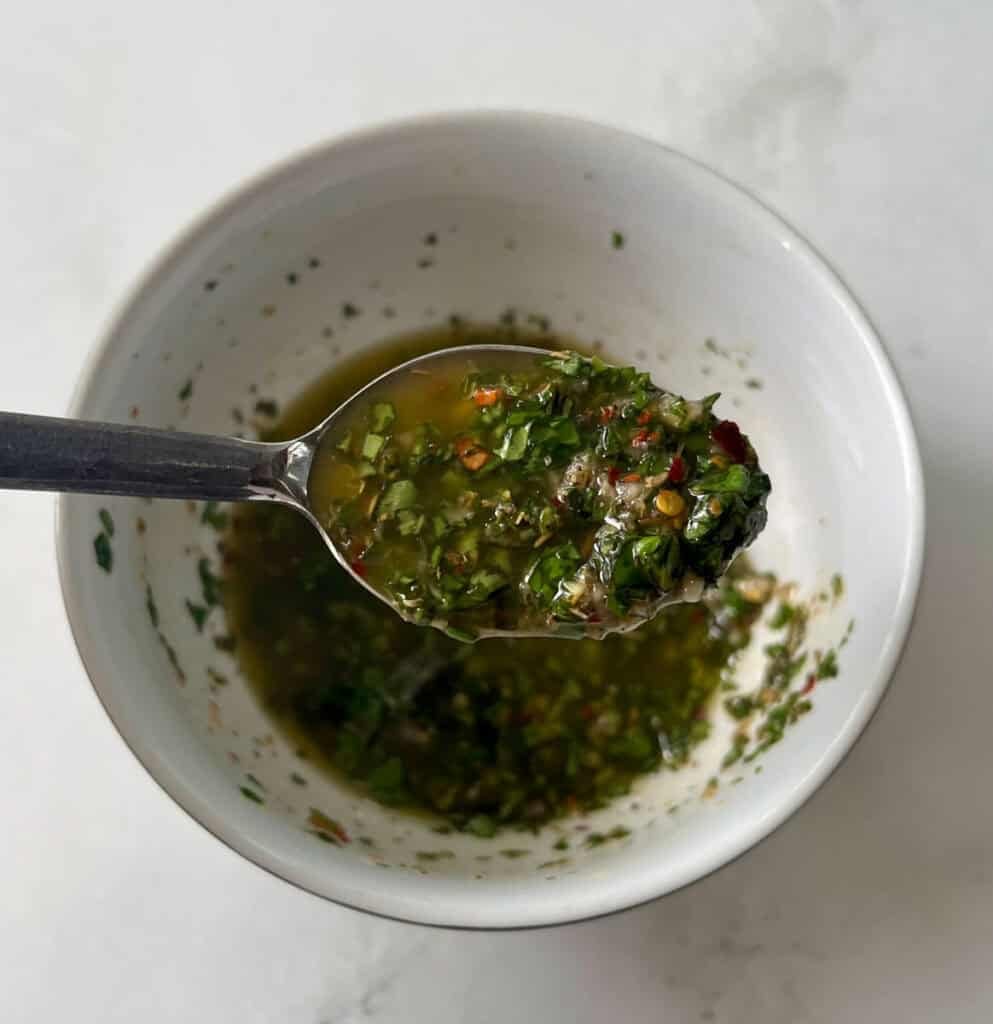 Close-up of green salsa with herbs and spices in a white bowl.