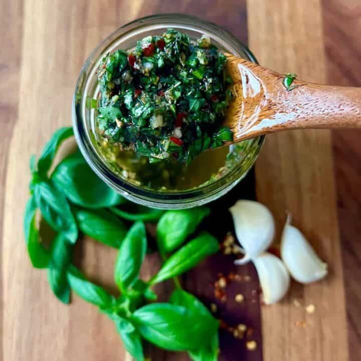 Close-up of basil pesto with garlic and fresh basil leaves on wooden surface.